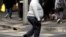 FILE - A man crosses a main road as pedestrians carrying food walk along the footpath in central Sydney, Australia.