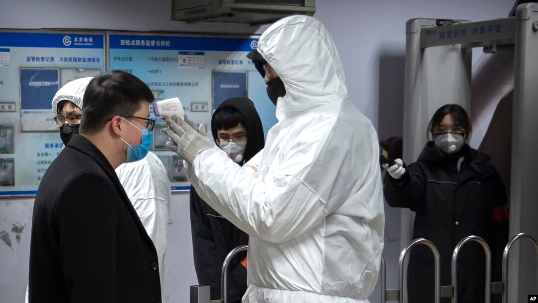 A worker wearing a hazardous materials suit takes the temperature of a passenger at the entrance to a subway station in Beijing, Jan. 26, 2020. 