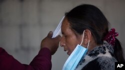Una mujer se detiene mientras una guía espiritual coloca velas cerca de su cabeza en el día de la fiesta del santo folklórico Maximón, en Guatemala, el miércoles 28 de octubre de 2020.