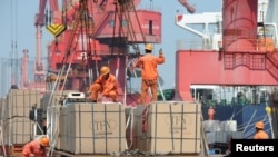 2019年6月7日，工人在中国江苏路连云港市的一个港口起重机上装载货物。（资料照）