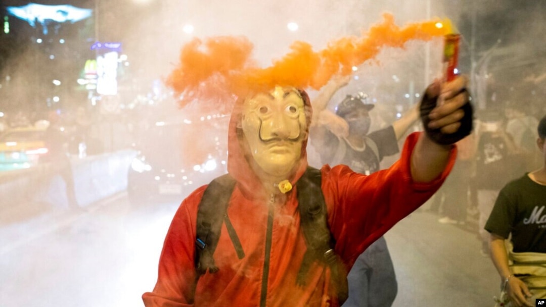 A protester wearing a mask holds a firework during a rally outside the headquarters of the Siam Commercial Bank, a publicly-held company in which the Thai king is the biggest shareholder, in Bangkok Thailand, Nov. 25, 2020.