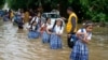 Para pelajar berpegangan pada tali saat menyeberangi jalan yang banjir setelah hujan lebat, dalam perjalanan pulang sekolah di kota Ajmer, India. (AP)&nbsp;