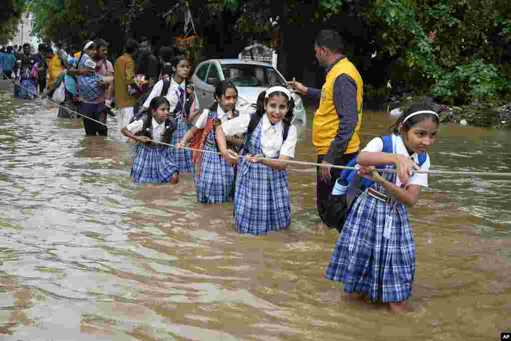 Para pelajar berpegangan pada tali saat menyeberangi jalan yang banjir setelah hujan lebat, dalam perjalanan pulang sekolah di kota Ajmer, India. (AP)&nbsp;