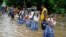 Para pelajar berpegangan pada tali saat menyeberangi jalan yang banjir setelah hujan lebat, dalam perjalanan pulang sekolah di kota Ajmer, India. (AP)&nbsp;