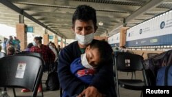 A migrant who crossed Gateway International Bridge from Mexico to be processed to seek asylum in the U.S., waits with a child at a bus terminal to head to their destination, in Brownsville, Texas, Feb. 25, 2021. 