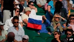 Penonton yang memegang bendera Rusia menyaksikan pertandingan putaran ketiga tunggal putra antara Daniil Medvedev dari Rusia dan Marin Cilic dari Kroasia di London, Sabtu 3 Juli 2021. (Foto: AP)