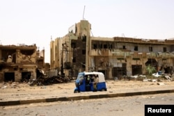 People pass by damaged cars and buildings at the central market during clashes between the paramilitary Rapid Support Forces and the army in Khartoum on April 27, 2023. (Mohamed Nureldin Abdallah/Reuters)