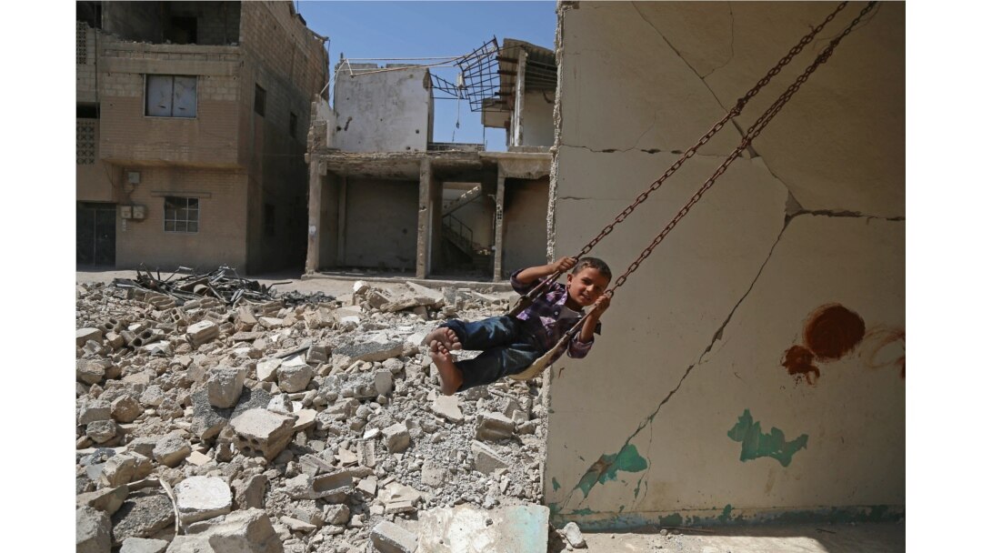 FILE - A Syrian boy plays on a swing in a destroyed building in the rebel-held town of Douma, on the eastern outskirts of Damascus, Sept. 3, 2017.