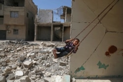 FILE - A Syrian boy plays on a swing in a destroyed building in the rebel-held town of Douma, on the eastern outskirts of Damascus, Sept. 3, 2017.