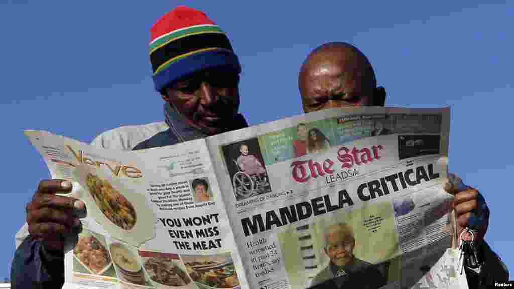 Men read a newspaper next to a stall in Soweto.