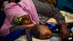 FILE - A mother sleeps with her child holding a toy gun, outside the UN refugee agency in Cape Town, South Africa, Oct. 10, 2019.