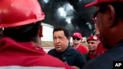 El presidente venezolano Hugo Chávez conversa con trabajadores de PDVSA mientras la refinería de Amuay arde todavía en el fondo, el domingo 26 de agosto de 2012.