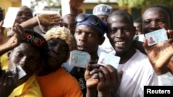 Men holds ID cards as they wait in line to register to vote in a polling station during elections in Kano, March 28, 2015. 