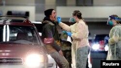 FILE - A person receives a throat swab from a health care worker at a drive-thru testing site inside the Bismarck Event Center as the COVID-19 outbreak continues in Bismarck, North Dakota, Oct. 26, 2020.