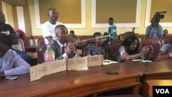 A Harare resident displays a sample of dirty water in a bottle next to him during a meeting with the city's mayor at a meeting at Town House, in Harare, Zimbabwe, Dec. 29, 2017. (S. Mhofu/VOA)