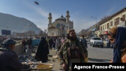 Seornag anggota pasukan Taliban berdiri di samping penjual makanan burung di salah satu pasar di Kabul, pada 3 Desember 2021. (Foto: AFP/Arman Sahel)