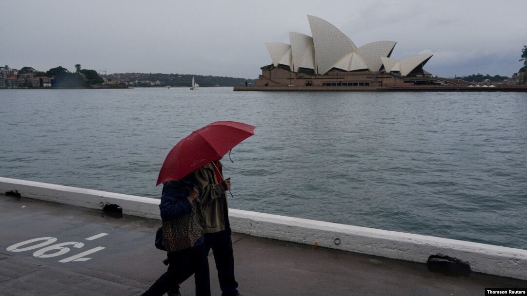 People share an umbrella while walking along the waterfront near the Sydney Opera House as eastern Australia experiences a winter cold front, in Sydney, Australia, June 10, 2021.