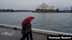 People share an umbrella while walking along the waterfront near the Sydney Opera House as eastern Australia experiences a winter cold front, in Sydney, Australia, June 10, 2021.
