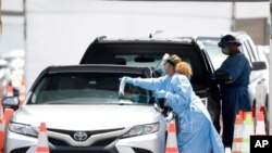 FILE - Health care workers prepare to test drivers at a drive-through coronavirus testing site outside of Hard Rock Stadium, June 26, 2020, in Miami Gardens, Florida.