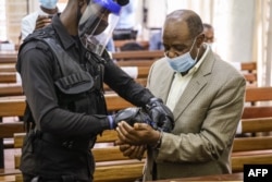 FILE—"Hotel Rwanda" hero Paul Rusesabagina (R) is handcuffed by a police officer after his pre-trial court session at the Kicukiro Primary court in Kigali, Rwanda, on September 14, 2020.