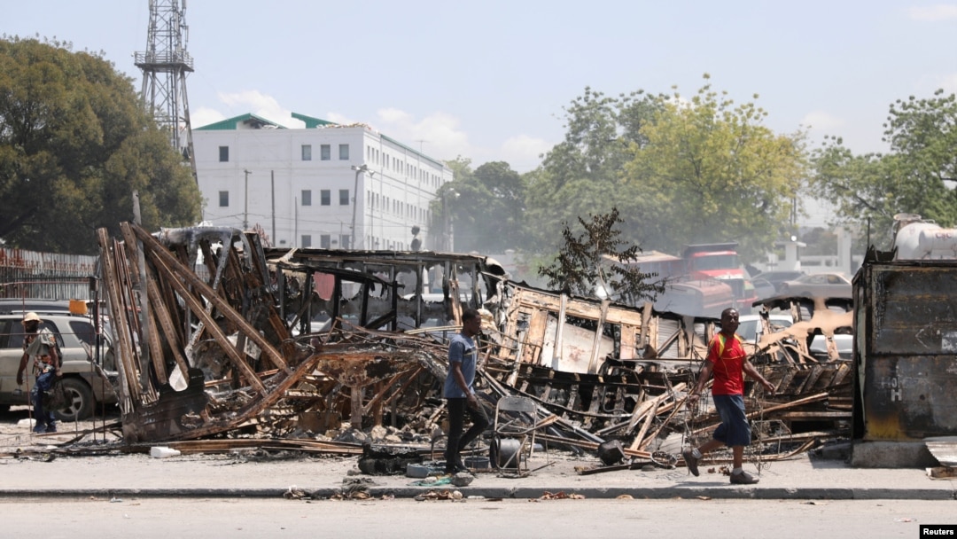 ARCHIVO - Personas caminan cerca del palacio presidencial junto a restos de vehículos incendiados por pandillas, mientras la violencia se extiende y las pandillas armadas amplían su control sobre la capital, en Puerto Príncipe, el 25 de marzo de 2024.
