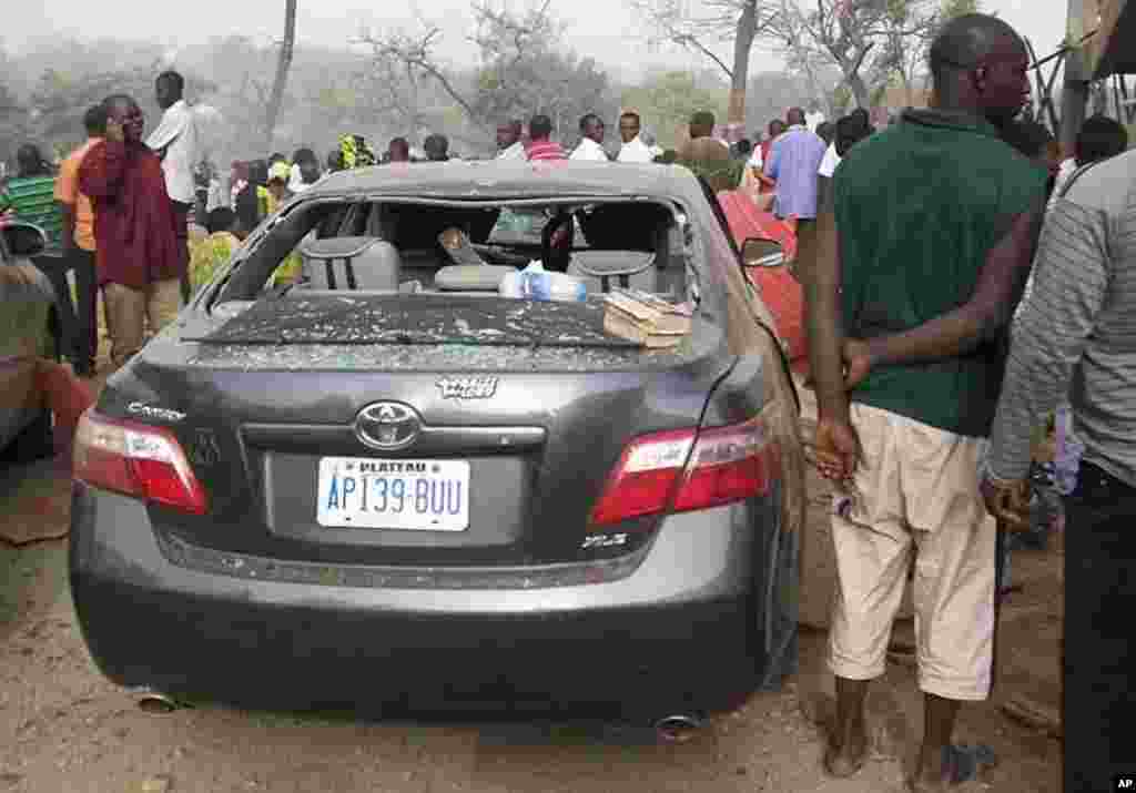 People stand by a damaged vehicle at a church, the site of a bomb blast, in Nigeria's central city of Jos February 26, 2012.