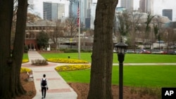 FILE - In this March 11, 2016, file photo, a pedestrian walks through the Georgia Tech campus as the downtown Atlanta skyline looms in the background.