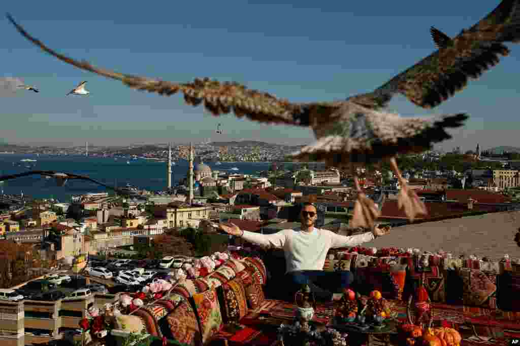 A seagull files over a man sitting at a coffee shop backdropped by the Bosporus Strait in Istanbul, Turkey.
