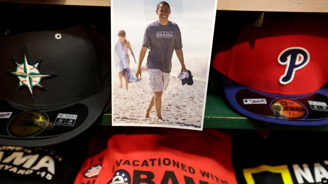 A photograph of President Barack Obama, top, is attached to a shelf near hats and souvenir clothing in a shop, Aug. 6, 2015, in Oak Bluffs, Mass., on the island of Martha's Vineyard. 
