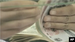 A bank teller counts a stack of US and Chinese currency.