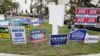 FILE - Campaign signs are posted near the Supervisor of Elections Office polling station while people line up for early voting in Pinellas County ahead of the election in Largo, Florida., Oct. 21, 2020. 