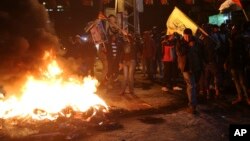 Palestinos queman llantas mientras ondean banderas palestinas y fotos del fallecido presidente palestino Yasser Arafat durante una protesta en Gaza, por la decisión del presidente Trump sobre Jerusalén, el miércoles, 6 de diciembre de 2017.