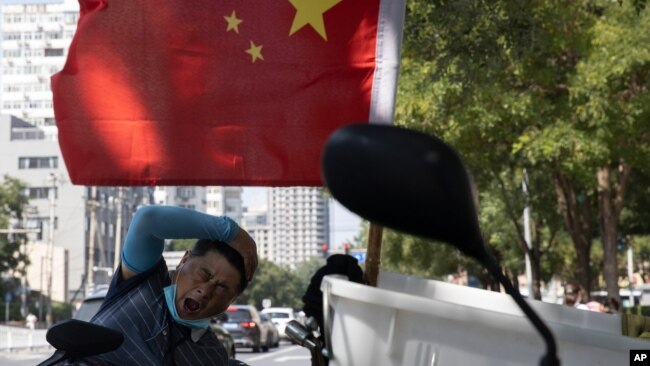 北京街头一名快递员在电动车旁休息放松。(2020年9月2日)