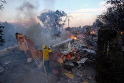 A firefighter tries to extinguish the flames at a burning house as the South Fire burns in Lytle Creek, San Bernardino County, north of Rialto, Calif., Aug. 25, 2021.