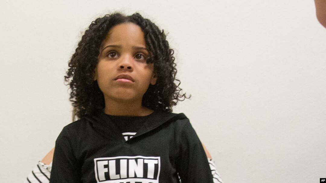Mari Copeny, 8 tuổi, đến từ Flint, tiểu bang Michigan, ngồi trên đùi của mẹ bé, bà Lulu Brezzell, khi họ cùng các cư dân Flint khác và những người ủng hộ chờ đợi bên ngoài căn phòng Thống đốc bang Michigan Rick Snyder và Người điều hành EPA Gina McCarthy làm chứng trong một buổi điều trần của Quốc hội về cuộc khủng hoảng nước, ngày 17 tháng 3 năm 2016.
