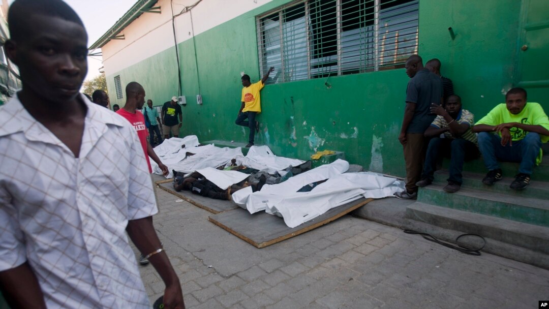 People walk past the bodies of victims who died during a carnival parade, lined up outside the morgue at the General Hospital in Port-au-Prince, Haiti, Feb. 17, 2015. 