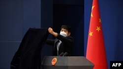 FILE - A worker wearing protective mask against the coronavirus covers the podium after the daily media briefing at the Foreign Ministry in Beijing, China, March 18, 2020. 