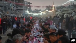 Warga Palestina duduk di meja besar yang dikelilingi reruntuhan rumah dan bangunan yang hancur saat mereka berkumpul untuk berbuka puasa pada hari pertama Ramadan di Rafah, Jalur Gaza selatan, Sabtu, 1 Maret 2025 (Abdel Kareem Hana/AP)