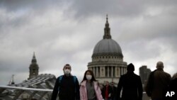 People wearing face masks walk across the Millennium footbridge backdropped by the dome of St Paul's Cathedral in London, March 10, 2020. 