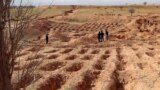 (FILE) Libyans walk around graves dug on the ground from which bodies were recovered in the western town Tarhuna on February 9, 2022.