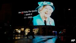 Seorang pria berjalan melewati gambar Ratu Elizabeth II yang diproyeksikan ke layar besar di kawasan Piccadilly Circus di London, Kamis, 8 September 2022.