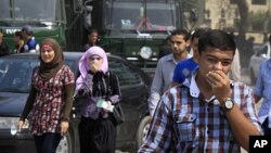 FILE - Egyptians cover their faces to avoid tear gas vapor as they walk at the site of clashes between protesters and anti-riot police near the Israeli Embassy in Cairo, Sept. 10, 2011.