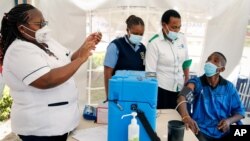 A nurse, left, prepares a shot of AstraZeneca COVID-19 vaccine, manufactured by the Serum Institute of India and provided through the global COVAX initiative, from a portable cold storage box, center, in Machakos, Kenya, March 24, 2021.