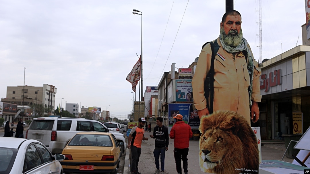 FILE - People pass by a poster of Ali Jayad al-Salhi, 65, a volunteer with Popular Mobilization Forces killed fighting Islamic State militants, in Basra, 340 miles (550 kilometers) southeast of Baghdad, Iraq, Nov. 26, 2017.