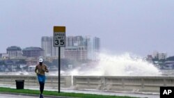 Un corredor se abre paso a lo largo de Bayshore Boulevard, en Tampa, Florida, mientras una ola rompe sobre un malecón, durante las secuelas de la tormenta tropical Elsa el miércoles 7 de julio de 2021.