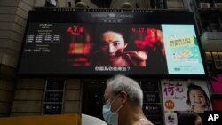 FILE-People walk past a huge TV screen showing movie listings "along a downtown street in Hong Kong, Sept. 17, 2020.