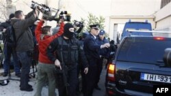 Greek police special forces secure the area as a police van with suspected members of the group Revolutionary Nuclei of Fire, background, enter the court set up inside a maximum security prison in Athens, Monday, Jan. 17, 2011. Nine suspected members of a