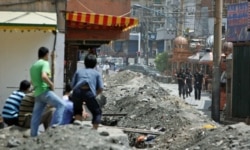 FILE - Ethnic Uighurs look on as Chinese security forces stand by the entrance to the Uighurs' neighborhood in Urumqi in China's Xinjiang autonomous region, July 8, 2009.