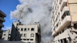 TOPSHOT - Palestinians watch as smoke rises from a building hit by an Israeli strike after a warning from the army to its occupants to evacuate the premises, in the Rimal neighbourhood of central Gaza City on August 21, 2024, amid the ongoing conflict bet