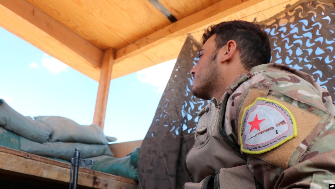 In this Oct. 7, 2019 file photo, a fighter from the U.S.-backed Kurdish-led Syrian Democratic Forces, SDF, stands guard inside a post where U.S. troops were based, in Tal Abyad town, at the Syrian-Turkish border, Syria.
